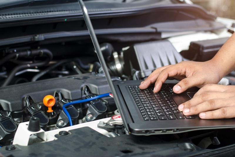 laptop leżący na silniku na którym ktoś pracuje